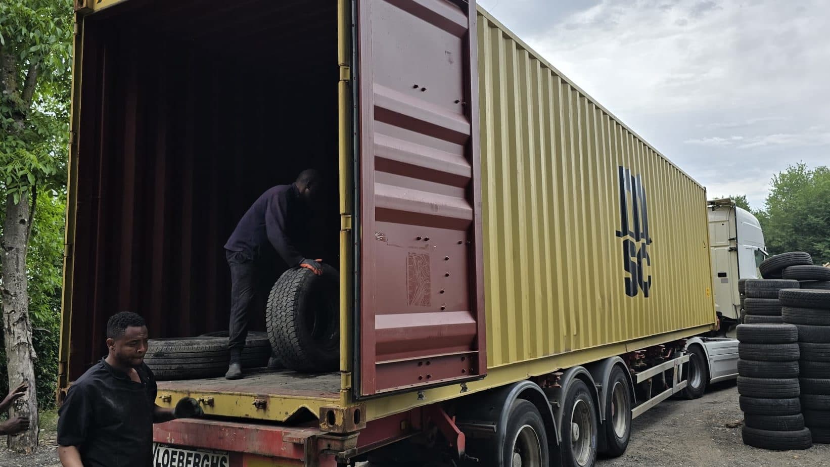 Two workers loading tyres into an open shipping container