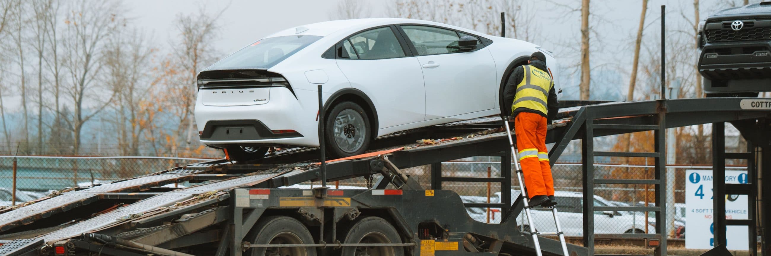 Car lashed onto a car-carrier trailer, an operator in a safety vest near the ramp